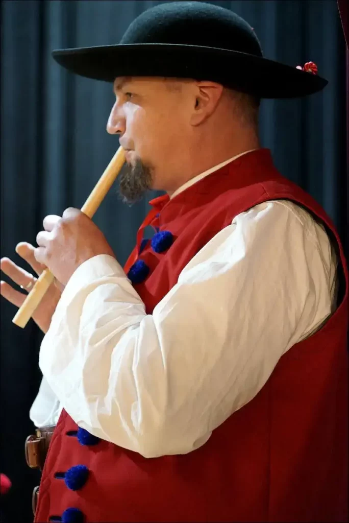 Mężczyzny w stroju ludowym górali dorzecza Soły, który gra na instrumencie podobnym do fletu.
