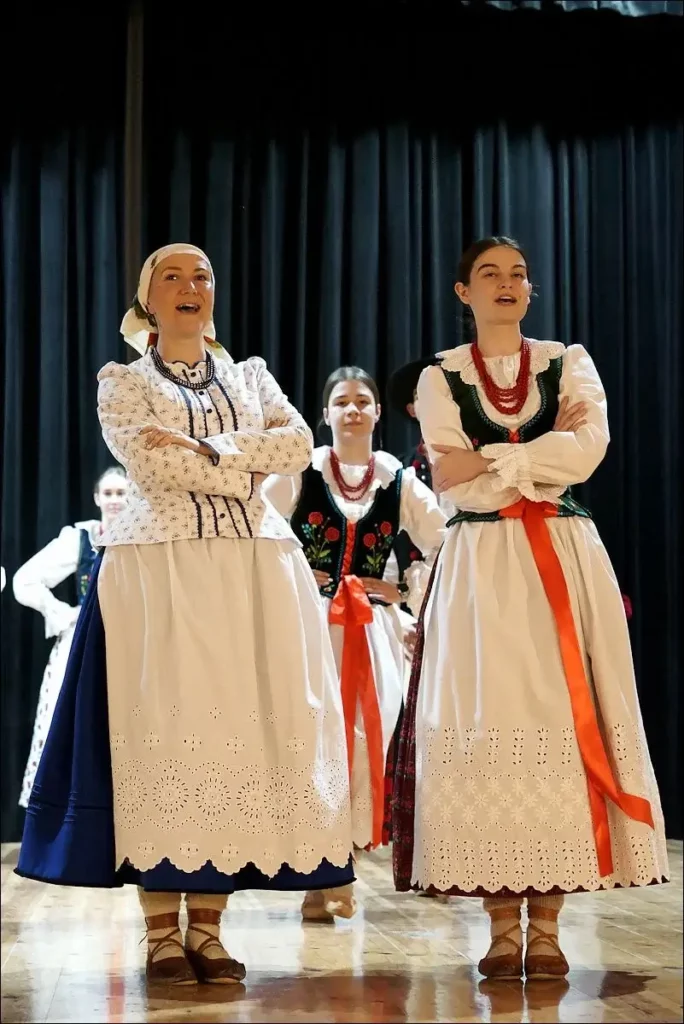 Cztery kobiety i jeden mężczyzna w tle. Wszyscy mają na sobie stroje ludowe górali dorzecza soły. Są w trakcie występu na scenie.