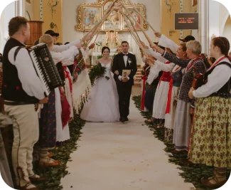 Para młoda idącą przez Kościół pod szpalerem ślubnym tworzonym przez palice Górali Żywieckich w ludowych strojach.