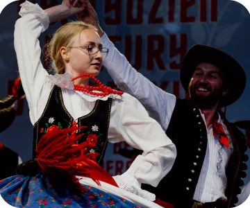 Górale dorzecza Soły podczas tańca. Mają na sobie barwne stroje ludowe, kamera jest do nich przybliżona i doskonale widać ruch czerwonych korali na szyi góralki.